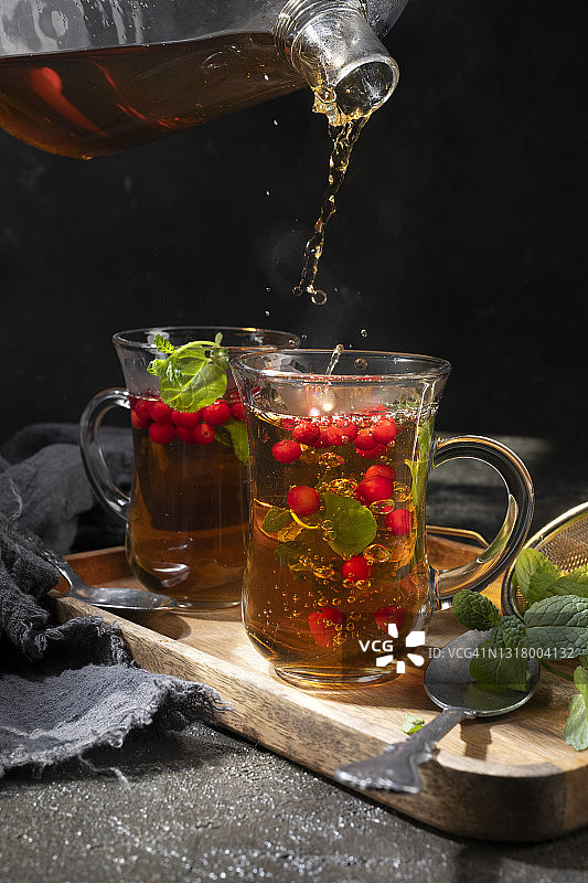 将红茶从透明茶壶中倒入黑色背景的杯子中图片素材