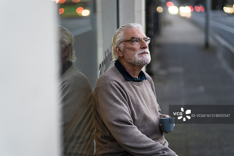 年长的男人与杯子看向别处，而坐在外面的咖啡馆在街上图片素材