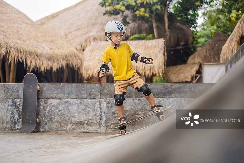 戴着头盔和护膝的运动男孩在滑板公园学习滑板。儿童教育、体育图片素材
