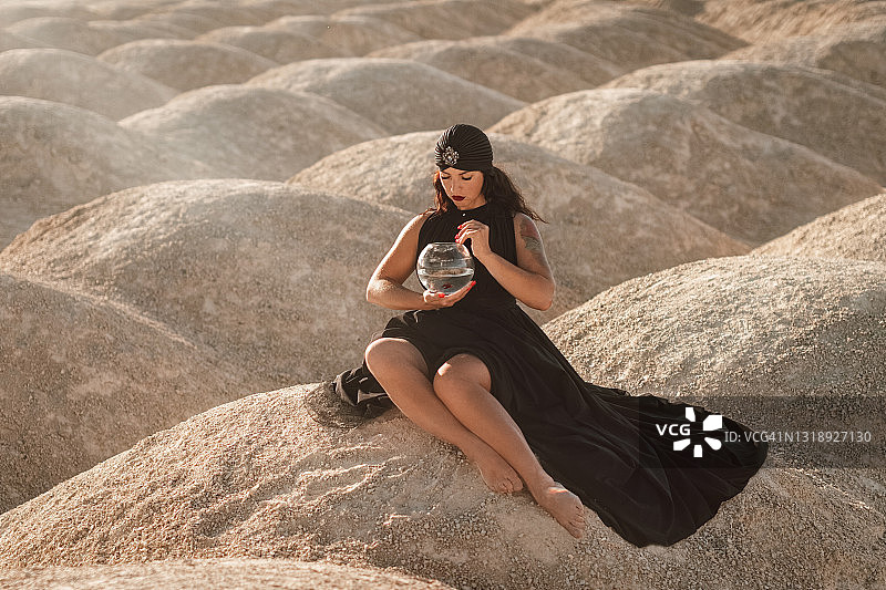 穿着黑裙、头缠黑巾、不穿鞋的女人坐在沙漠里图片素材
