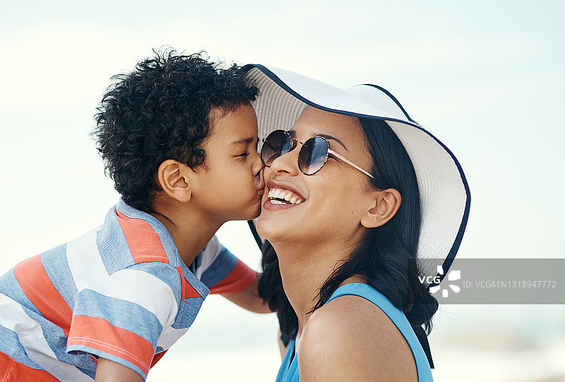 在海滩上，一位年轻的母亲被她的儿子亲吻脸颊图片素材