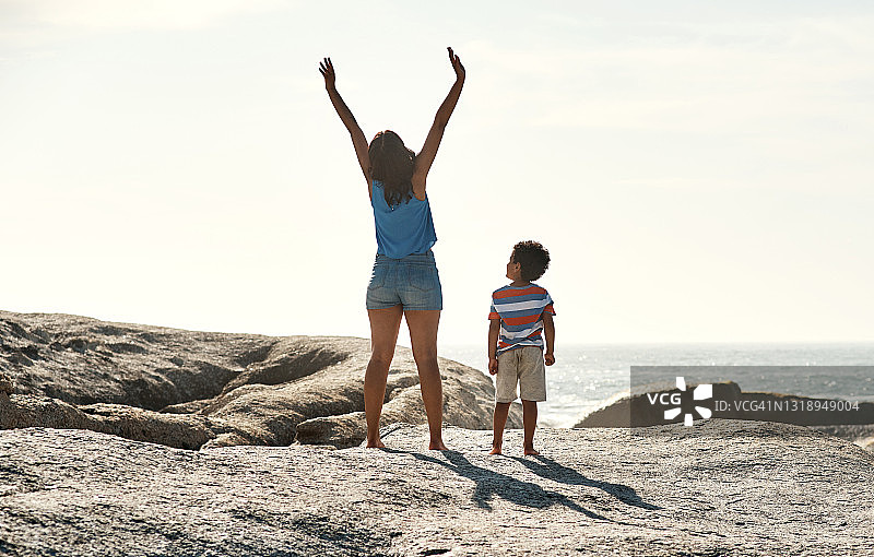 一个父母和他们的孩子在海滩的阳光下举起他们的手臂图片素材