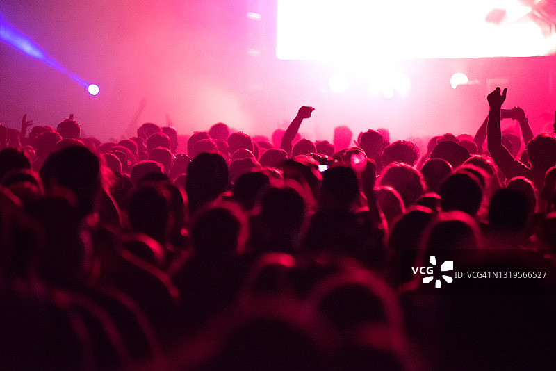 在音乐节上，一群人在红色的舞台灯光下举行现场音乐会图片素材