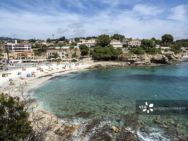 在西班牙的贝尼萨，一个小的白色沙滩被树木和日光浴的人包围。图片素材