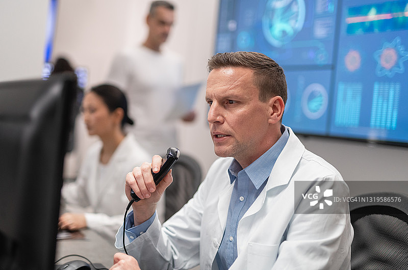 男性放射科医生一边看着核磁共振扫描一边对着听写记录器说话图片素材