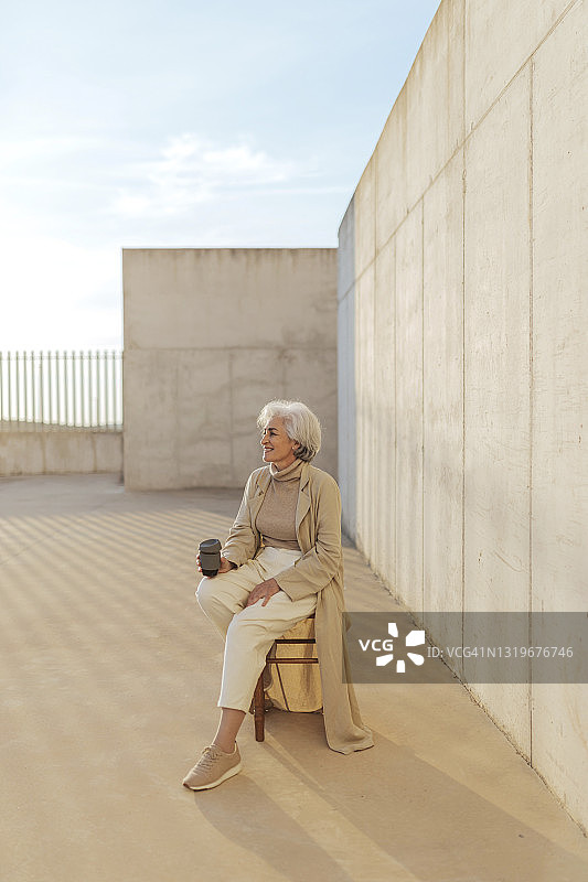 坐在凳子上，用可重复使用的咖啡杯看向别处的女人图片素材