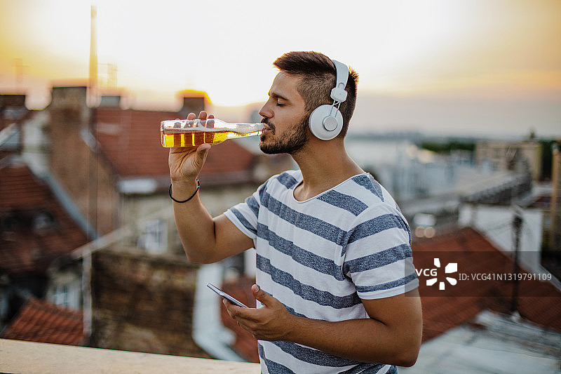 男人在屋顶上听音乐喝酒的肖像图片素材