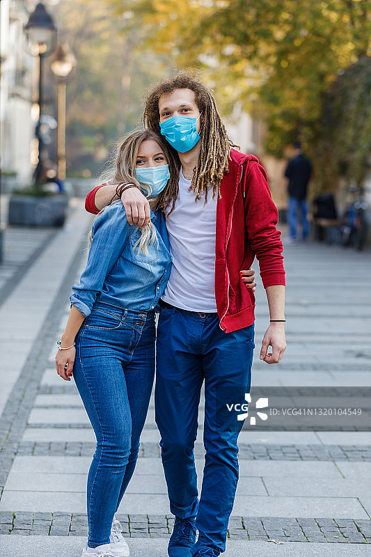 一对快乐的年轻情侣戴着面具在城市的街道上拥抱、亲吻，还聊得很开心。图片素材