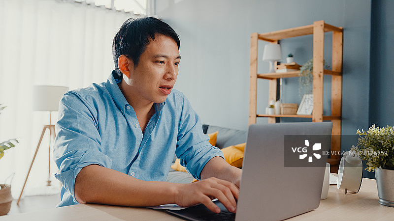 自由亚洲人随意穿用笔记本电脑在家里的客厅在线学习。图片素材