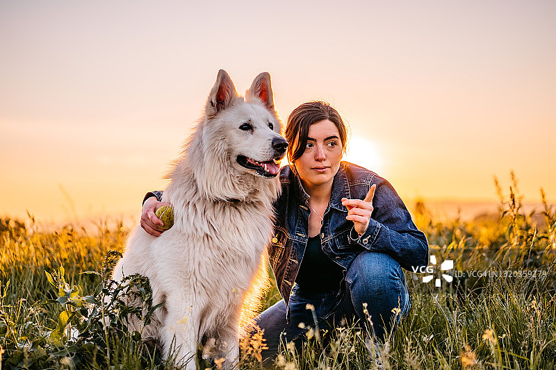 快乐的年轻女子和她的狗在草地上玩图片素材