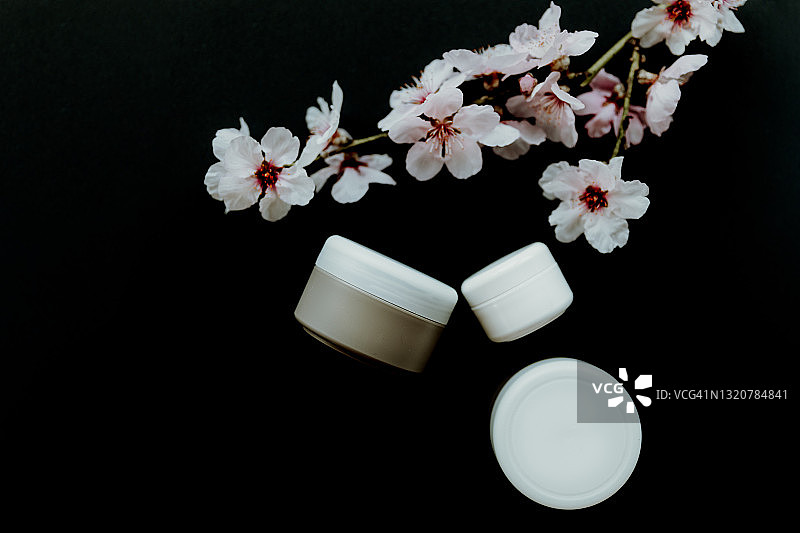 化妆品霜罐在黑色背景与白色杏花。图片素材