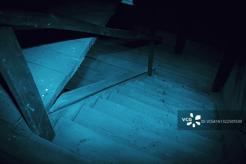 神秘恐怖的阁楼背景万圣节。古色古香的肮脏的木制楼梯在黑暗中神秘诡异的地下室或阁楼在蓝色月光下有着黑色的阴影图片素材