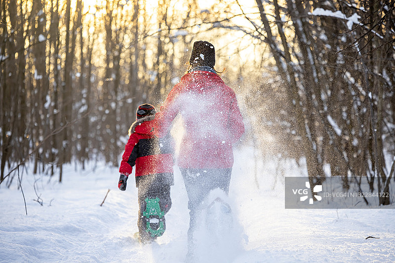 母亲和儿子跑与雪鞋在粉雪户外在冬天日落图片素材