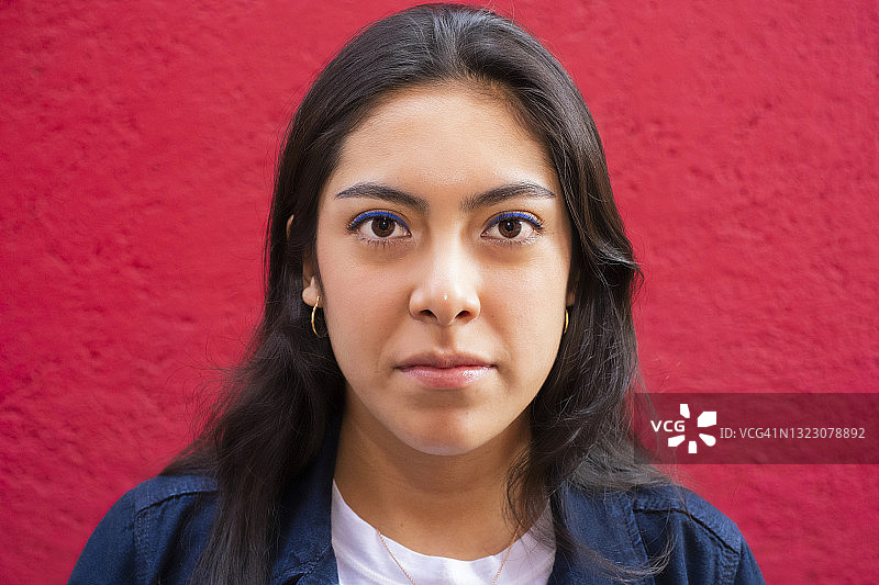年轻的拉丁裔妇女看着镜头，严肃的，红色的背景图片素材