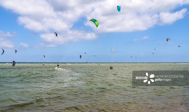 在一个阳光明媚的日子里，许多风筝冲浪活动在德国的波罗的海海滩拉博。图片素材
