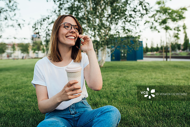 快乐的女孩在公园里喝咖啡，在电话里聊天图片素材