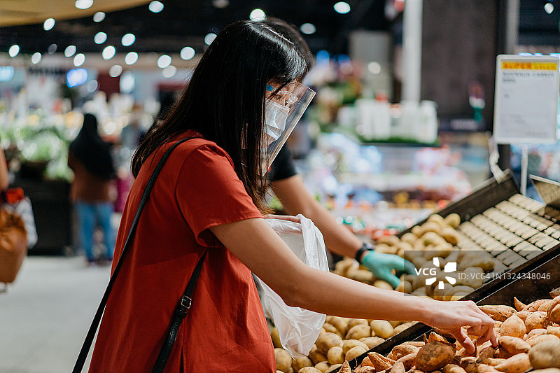 亚洲妇女戴着口罩和面罩在超市买土豆图片素材