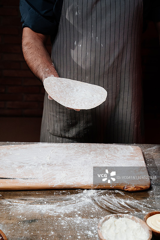 男人的手拿着一个薄薄的面饼。在家做披萨、面条或皮塔饼图片素材