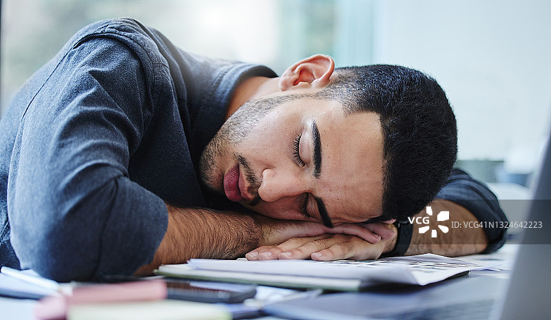 照片中，一位年轻的商人疲惫不堪，躺在办公室的桌子上睡着了图片素材