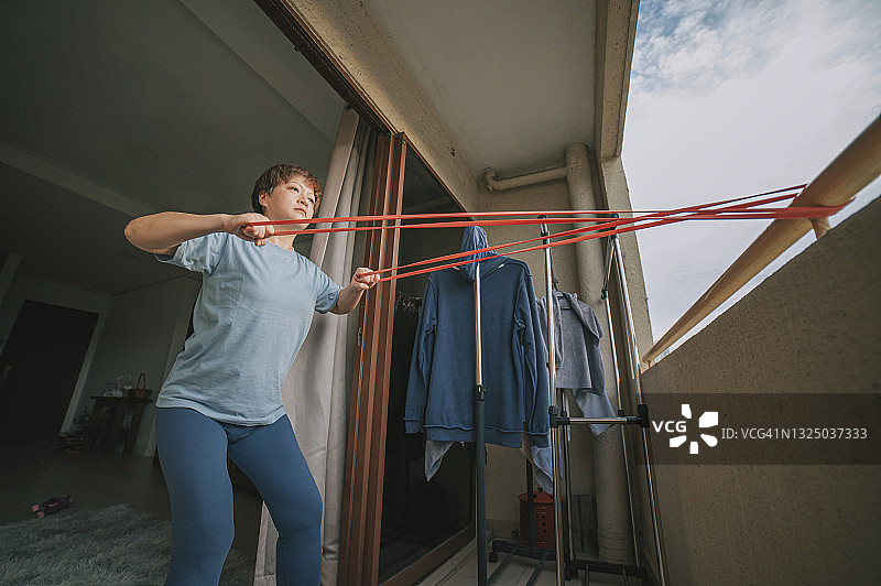 亚洲华人中年妇女使用抵抗带在阳台上进行家庭锻炼图片素材