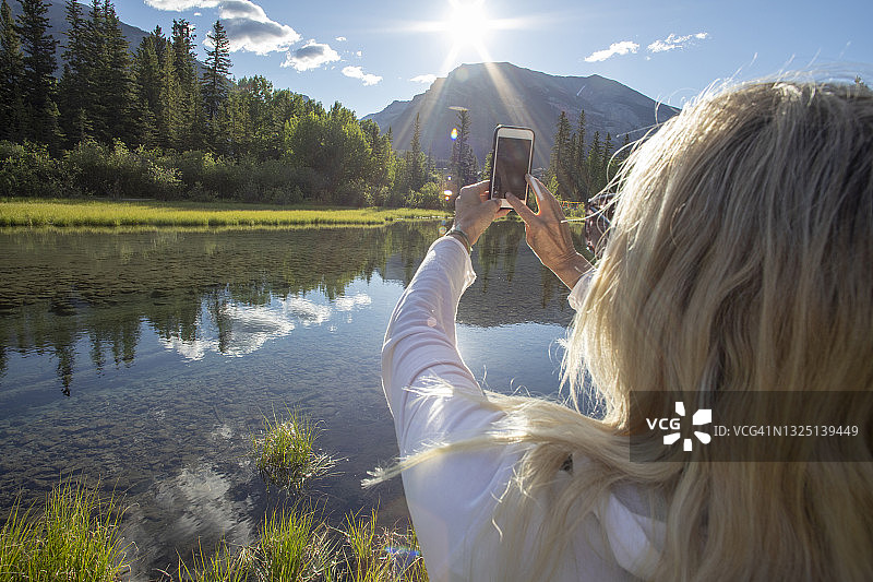 一名女性徒步旅行者在阳光明媚的湖滨用手机拍照图片素材