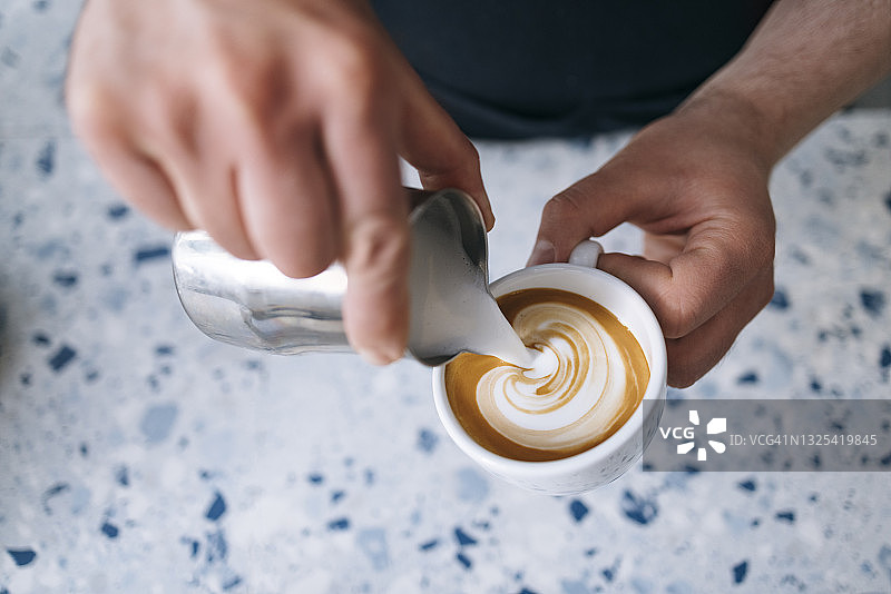 匿名咖啡师往一杯咖啡里倒牛奶泡沫图片素材