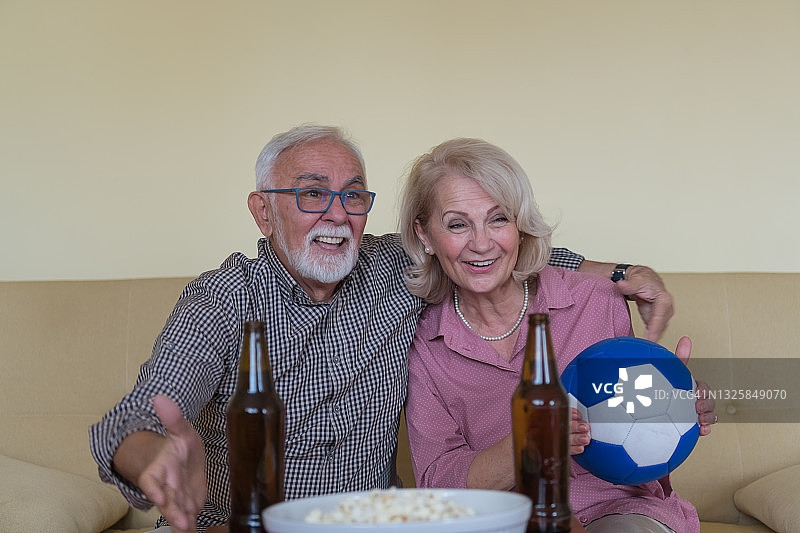 快乐的老夫妇正在家里看足球比赛。图片素材
