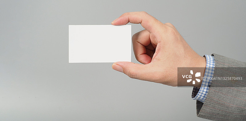 手握白色空白卡片，身穿灰色背景套装。企业人的概念图片素材