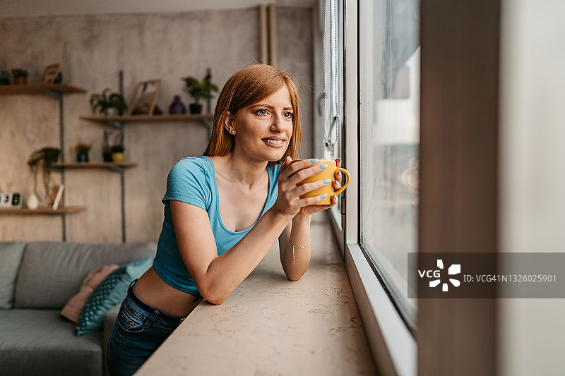 一个女人正从窗户往外看，喝着咖啡图片素材