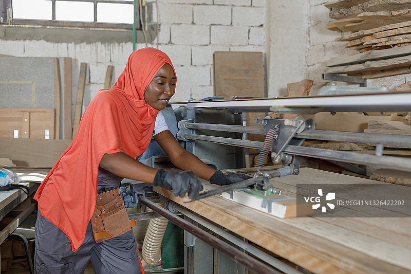 一名穆斯林妇女在木工制造的机器上打磨木头的照片。图片素材
