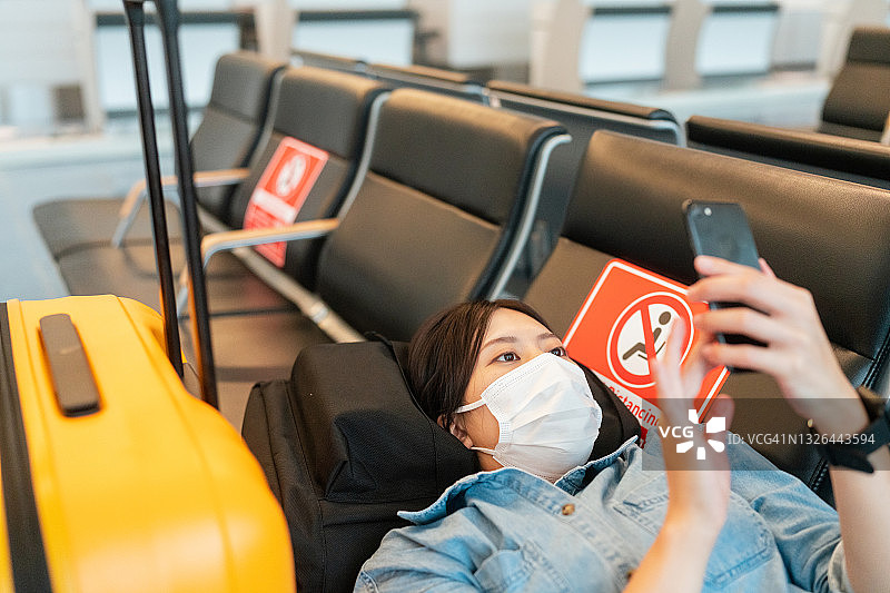 一名女游客一边用手机一边躺在椅子上等待航班图片素材