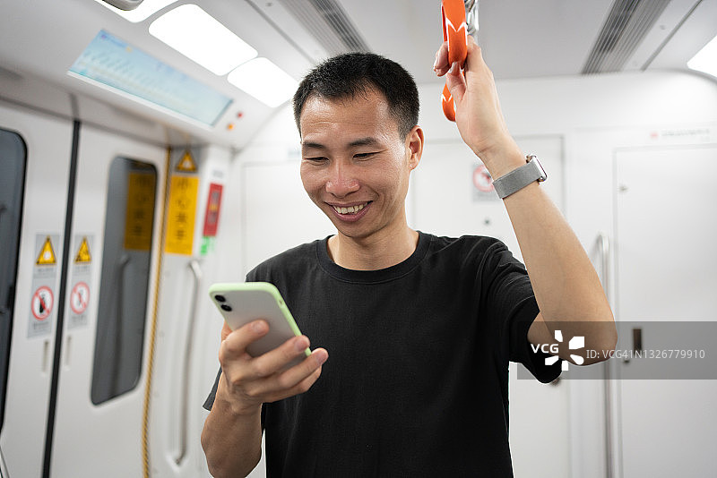 在地铁上看着智能手机的亚洲男人脸上挂着微笑图片素材