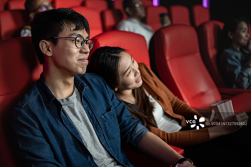 一对亚洲华人夫妇正在看电影，一边吃爆米花一边看电影图片素材