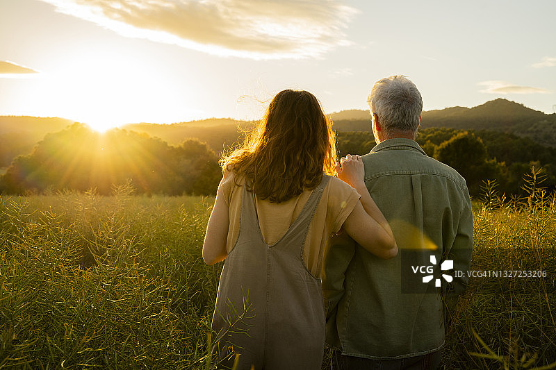 女儿和父亲站在田野里看日落的景色图片素材