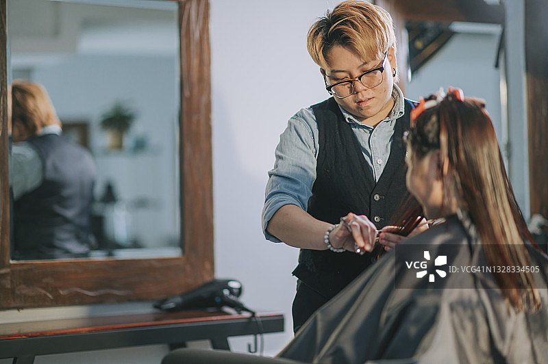 亚洲华人女发型师在美发沙龙为她的顾客理发图片素材