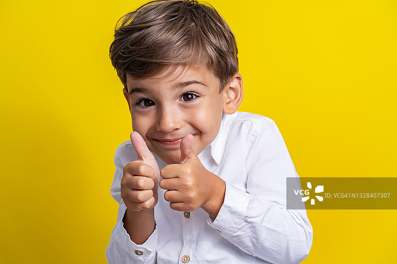 正面小白脸小男孩四岁时站在黄色背景的摄影棚前拍摄，微笑着举起大拇指支持孩子和成功的概念图片素材