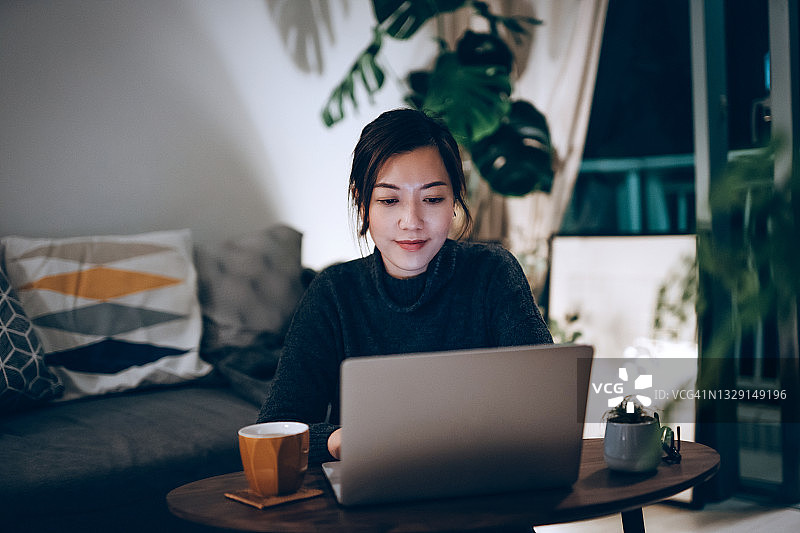 专注的年轻亚洲女性在家工作，在笔记本电脑上工作到深夜。家庭办公，创业，企业家和生活理念图片素材
