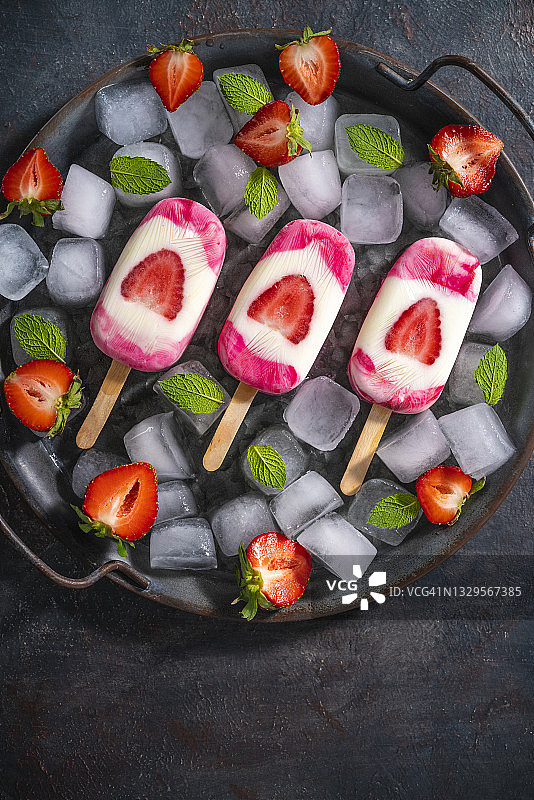 草莓自制冰棒与薄荷叶的冰块在平底锅的黑色背景图片素材