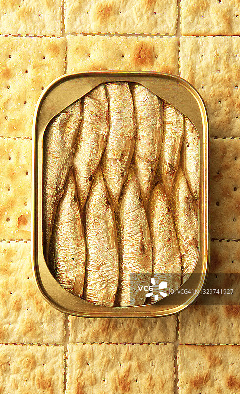 打开一个金色的罐头，里面装满橄榄油包装的小沙丁鱼，背景是咸饼干——系列的一部分图片素材