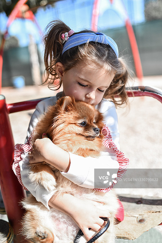 一个女孩和她的博美犬在操场上拥抱和放松图片素材