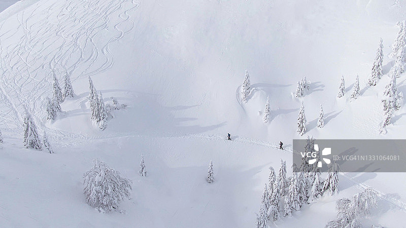 无人机:游客分乘飞机，沿着覆盖着粉末雪的斜坡徒步旅行。图片素材