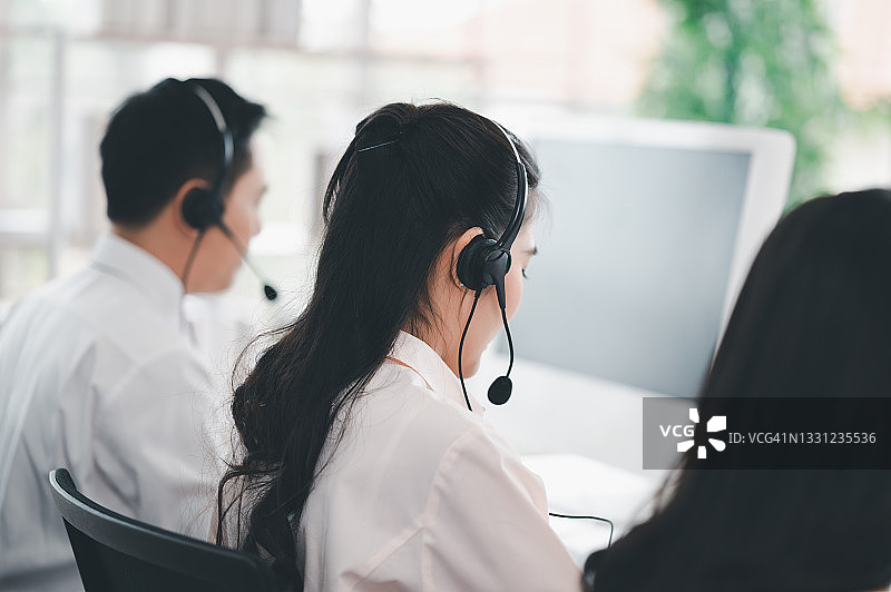 亚洲呼叫中心的员工带着耳机和麦克风。在柜台和电脑前为顾客服务时要微笑。服务理念与咨询。通信的概念。图片素材