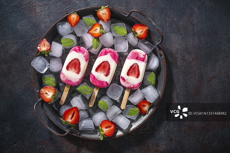 草莓自制冰棒与薄荷叶的冰块在平底锅黑暗的背景图片素材
