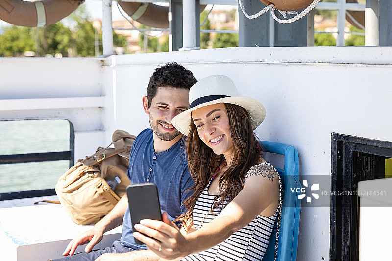 一名微笑的女子坐在游船上，用手机与一名男子自拍图片素材