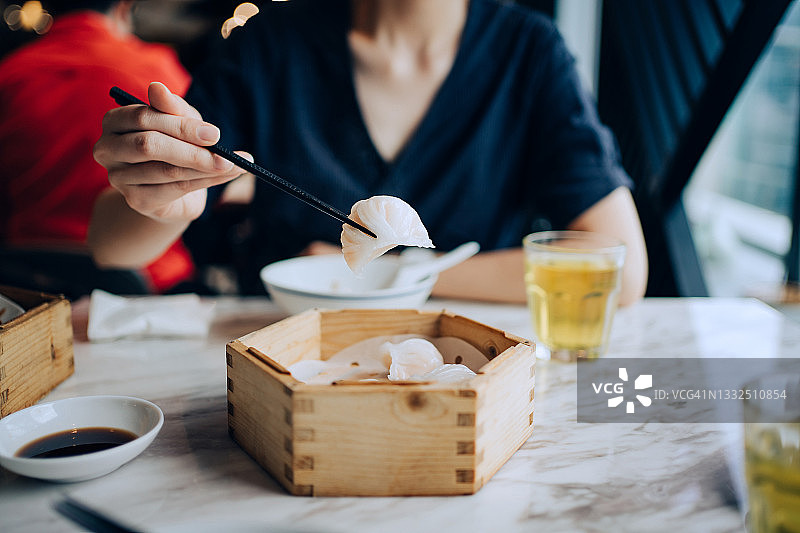 图为年轻的亚洲女子在餐馆的餐桌上，用竹制蒸笼端着茶，吃着传统的中国点心。中国美食和饮食文化。Yumcha。外出就餐的生活方式图片素材