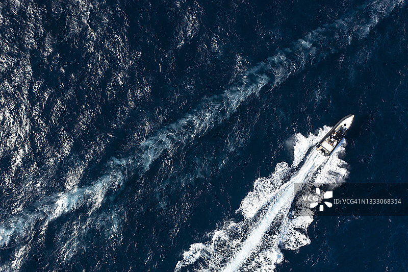 从上面看，令人惊叹的鸟瞰图，一艘船巡航在蓝色的水创造了一个尾流。意大利撒丁岛的翡翠海岸。图片素材
