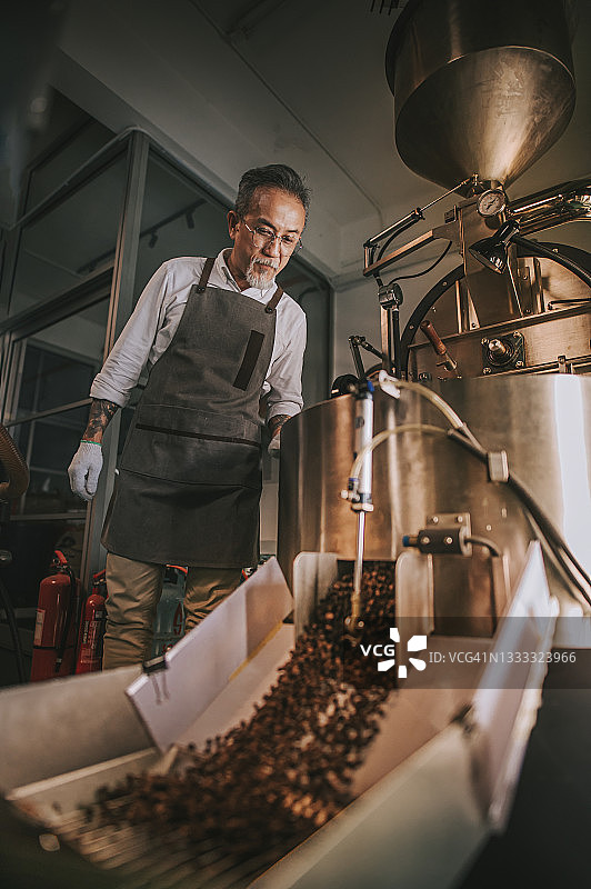 在他的工厂里，一名亚裔华裔年长的技工正在检查烘培咖啡豆的去石过程图片素材