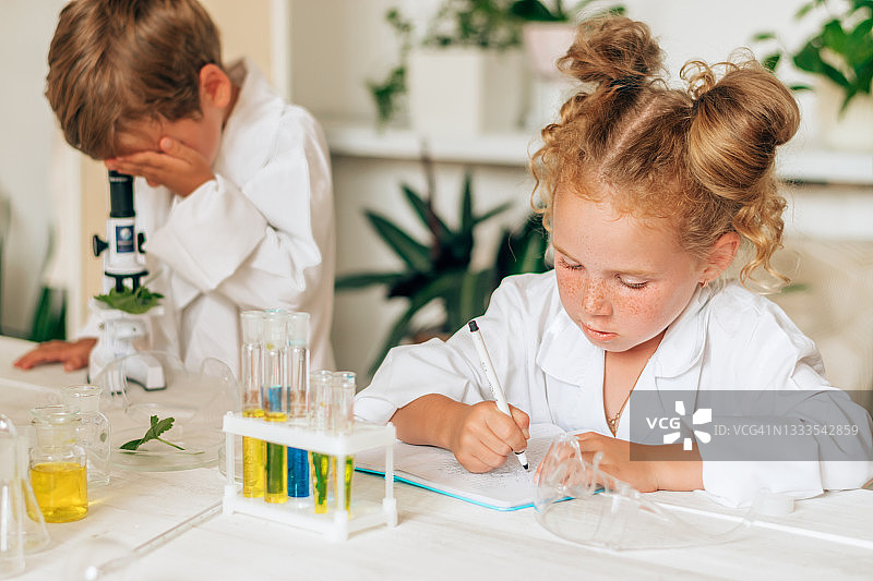 一个穿着白色制服的小男孩和小女孩在实验室里看着显微镜。回到学校的概念。年轻的科学家。自然科学。儿童的学前和学校教育图片素材