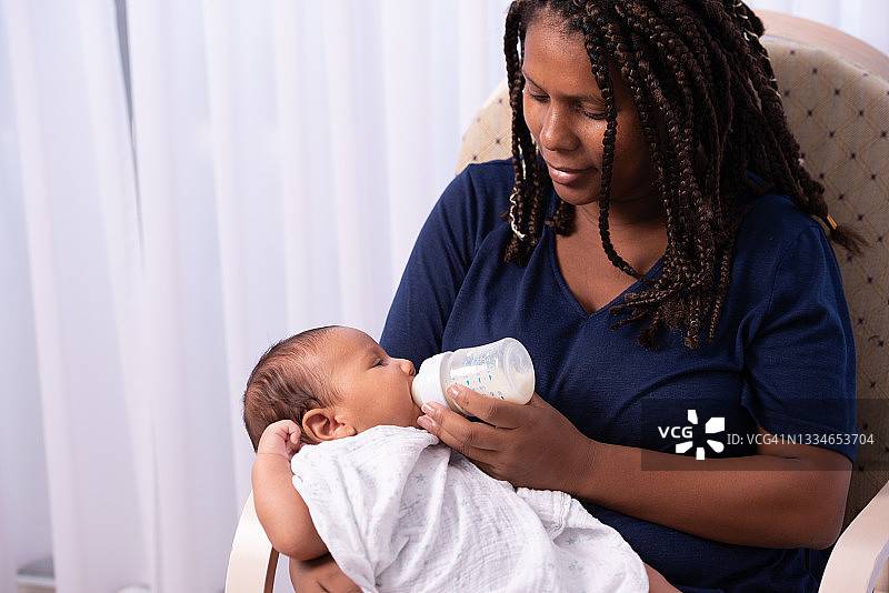 一个可爱的女婴在家里被她的妈妈用奶瓶喂养。图片素材