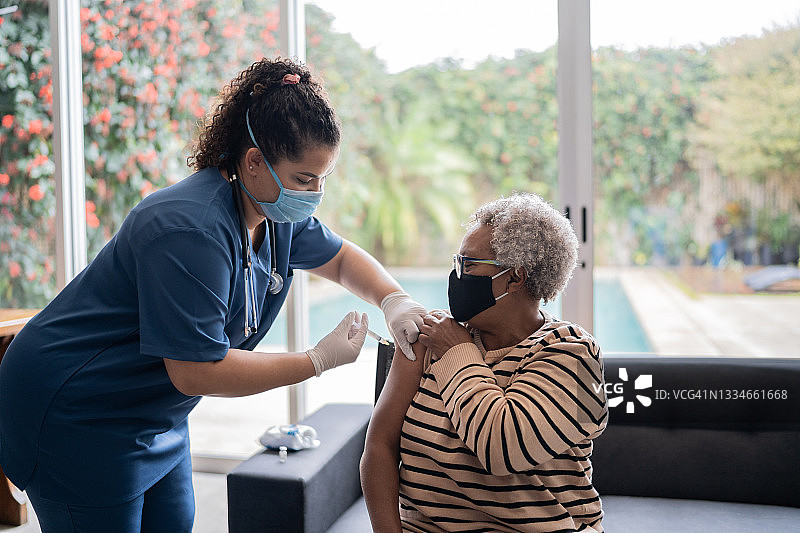 护理人员戴防护口罩在家给老年妇女接种疫苗图片素材
